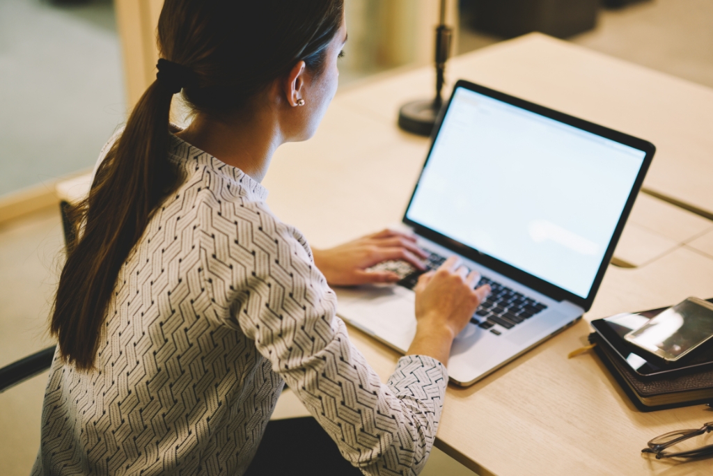 A woman is looking at a laptop screen while sitting at a table.