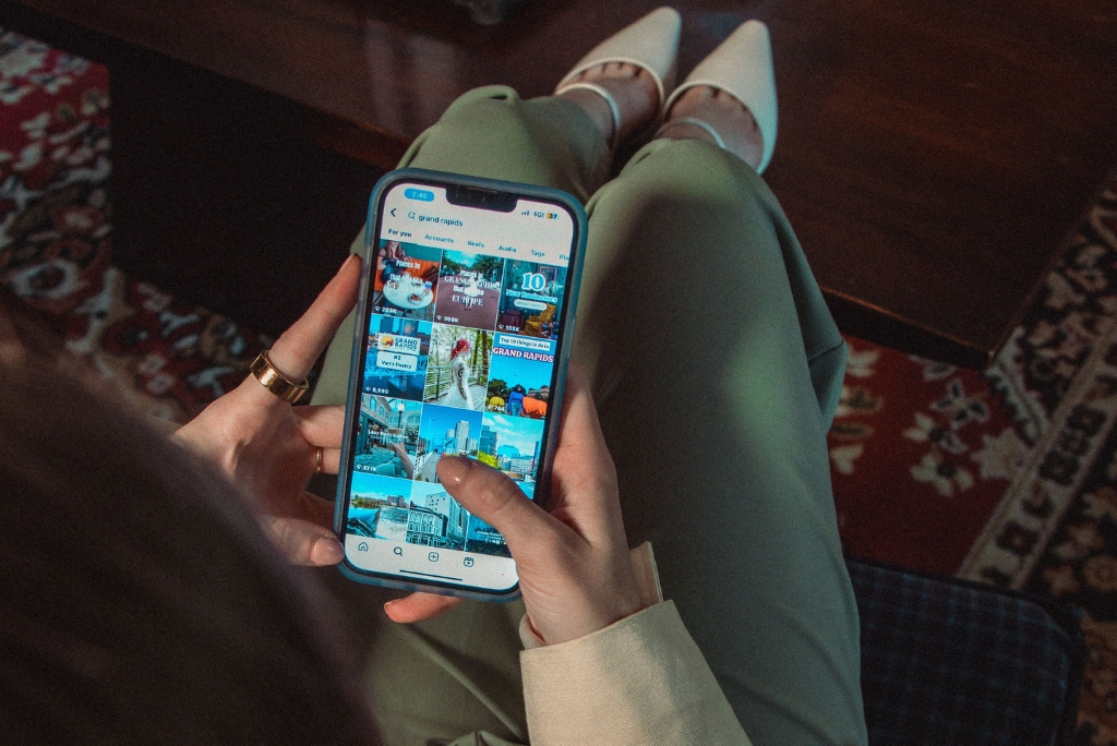 We see an over-the-shoulder point of view of someone holding an iPhone, scrolling on social media.