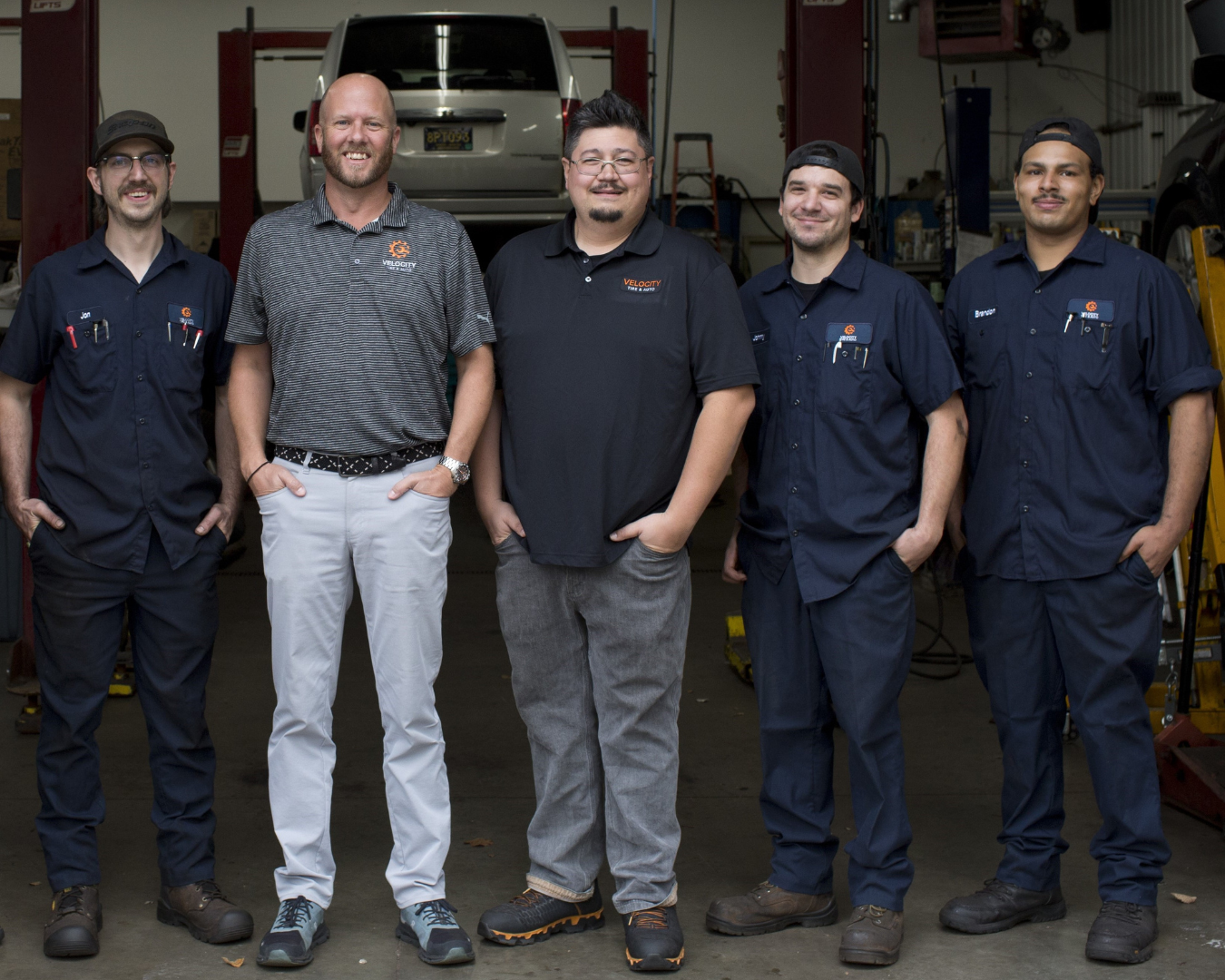 A group of 5 men stand smiling in front of an auto shop.